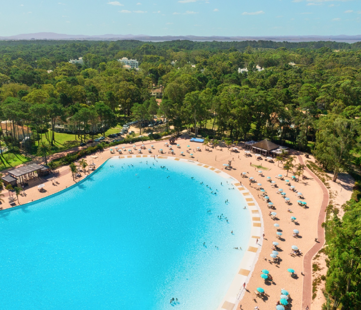 Vista aérea de Crystal Lagoons con playa, sombrillas y vegetación